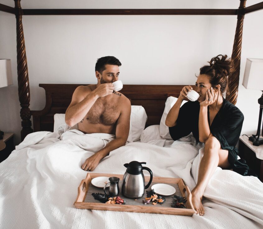 Smiling couple sitting on bed and drinking tea