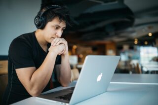 Picture of Man in black t-shirt sitting in coffee shop Wearing black Headphone and Using Macbook Pro