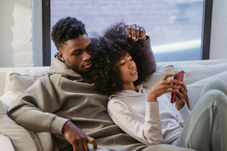 Picture of Young black couple resting together in home and using smartphone