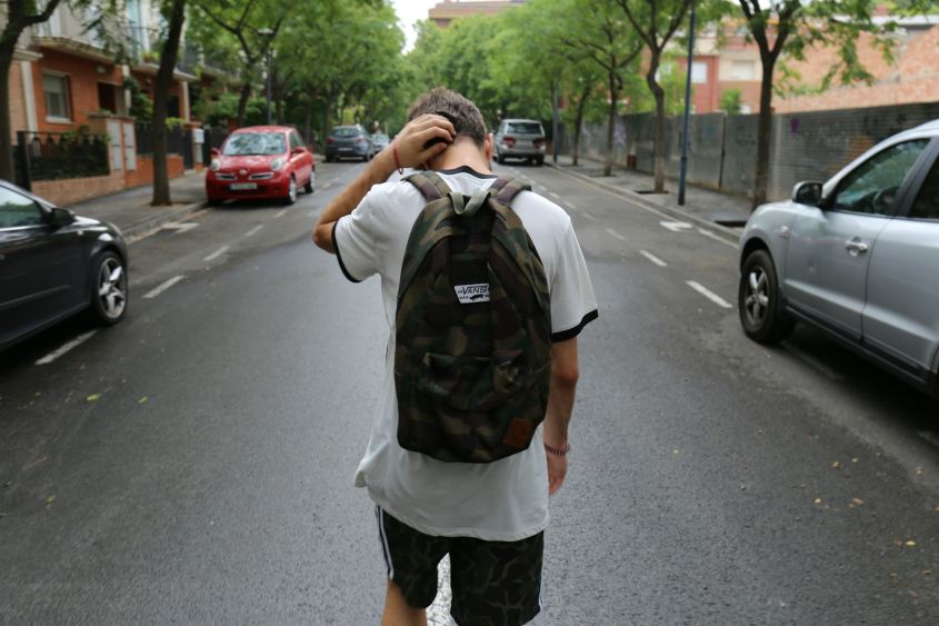 Picture of boy wearing white t-shirt and black shorts carrying backpack on the road